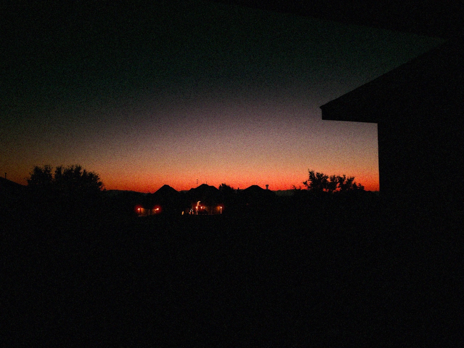 An orange sunrise above silhouetted rooftops and trees.